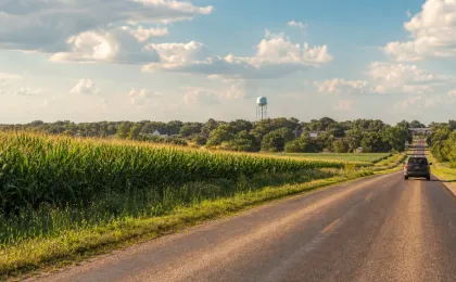 Summer Kansas county road beside green crop fields under a hot July sky.
